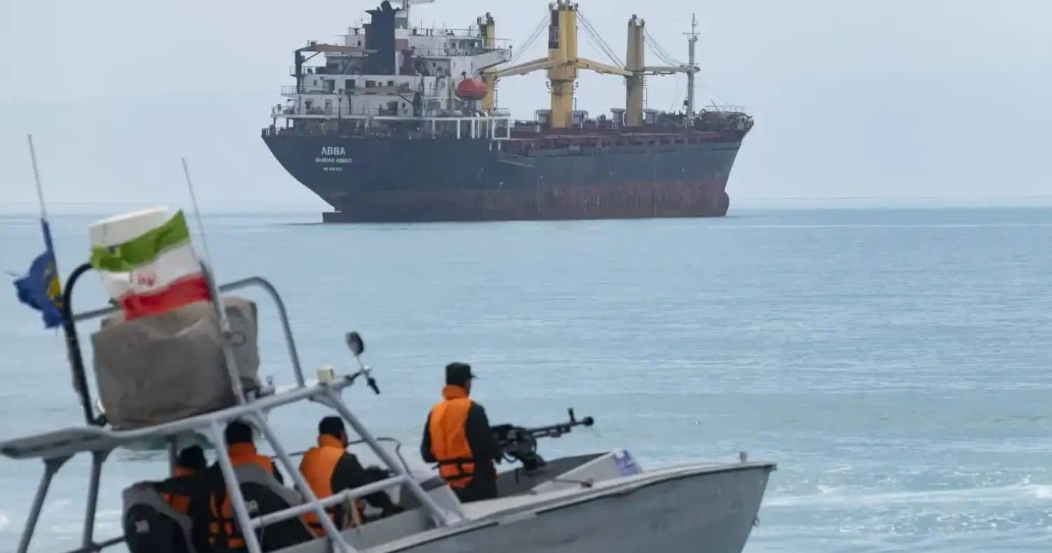 Iranian patrol boat with armed guards near a large cargo ship in the Strait of Hormuz. Iranian patrol boat with armed guards near a large cargo ship in the Strait of Hormuz.
